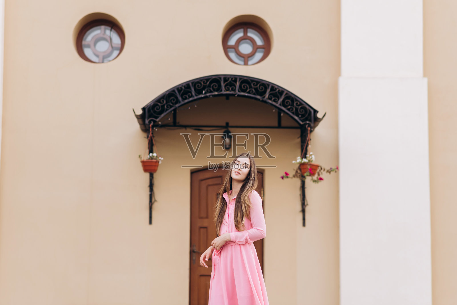 穿着粉红色长裙的漂亮女孩微笑着站在门口。照片摄影图片