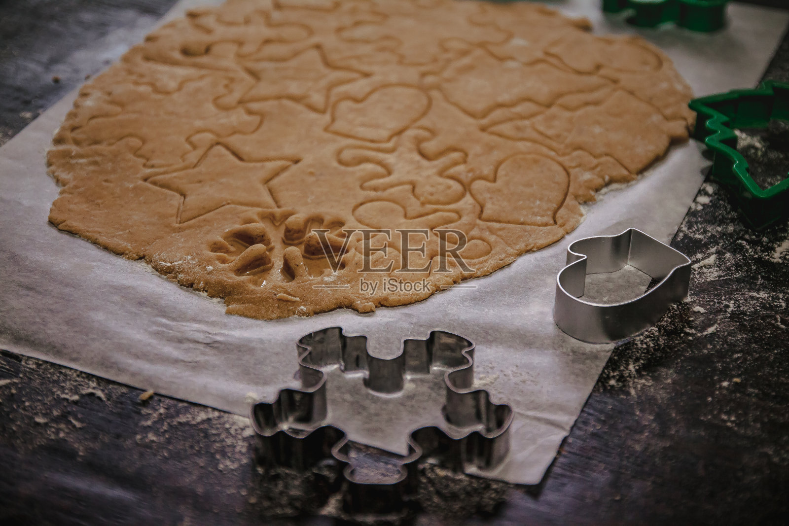 在烤盘纸上，以黑色为背景，从生面团中切出一棵圣诞树、星星、小矮人、心形的姜饼。前视图。节省空间照片摄影图片