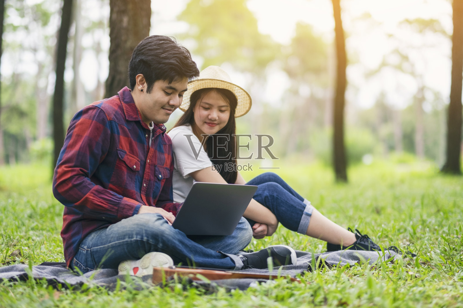 一对年轻夫妇坐在公园里看笔记本电脑照片摄影图片
