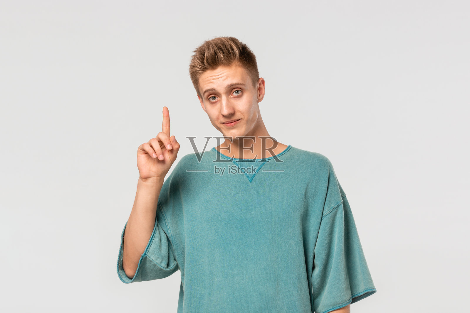 帅气的年轻人穿着绿色t恤，手指翘在广告的空白位置上。照片摄影图片