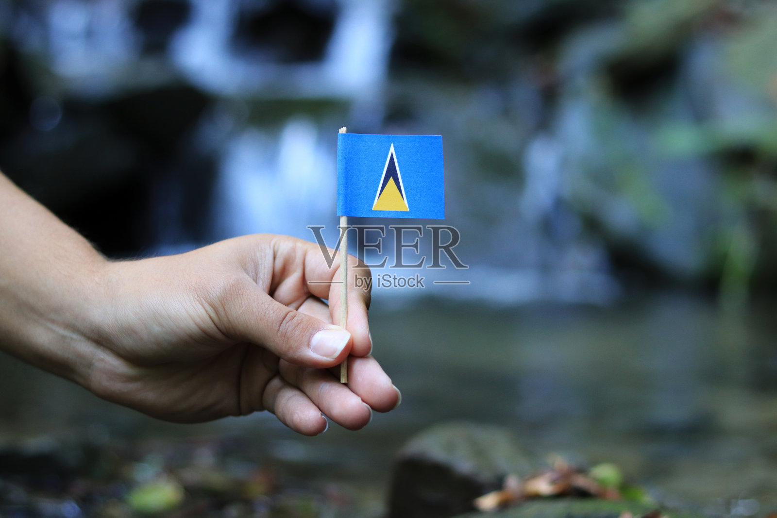 位于加勒比海的圣卢西亚国旗。一名少年手持木制的圣卢西亚国旗，背景是美丽的瀑布。自然与人性的概念照片摄影图片