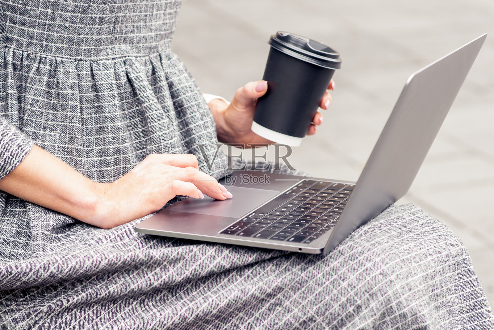 女性手近端着一杯咖啡在用笔记本电脑。照片摄影图片