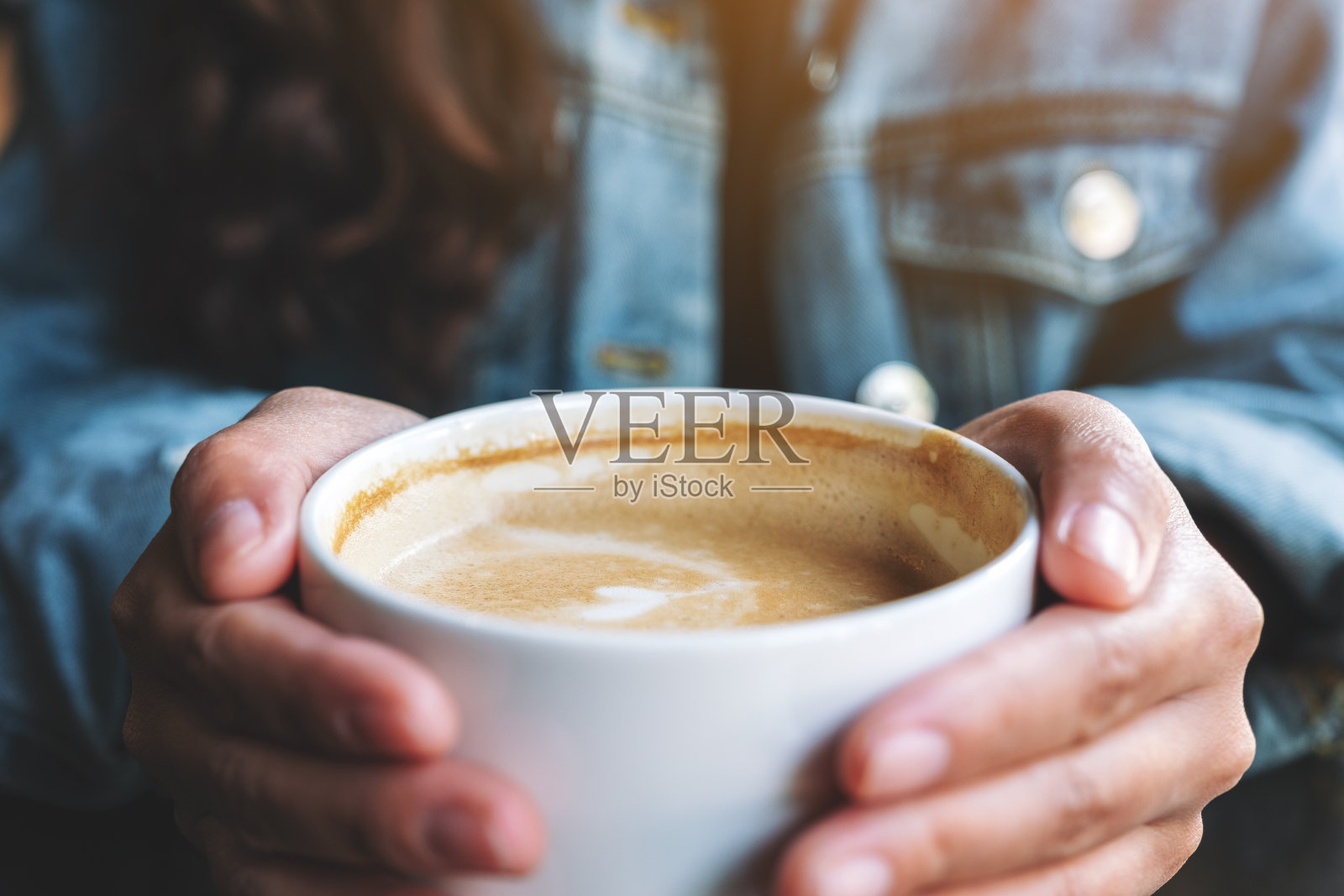 一个女人拿着一杯热拿铁咖啡放在桌子上照片摄影图片