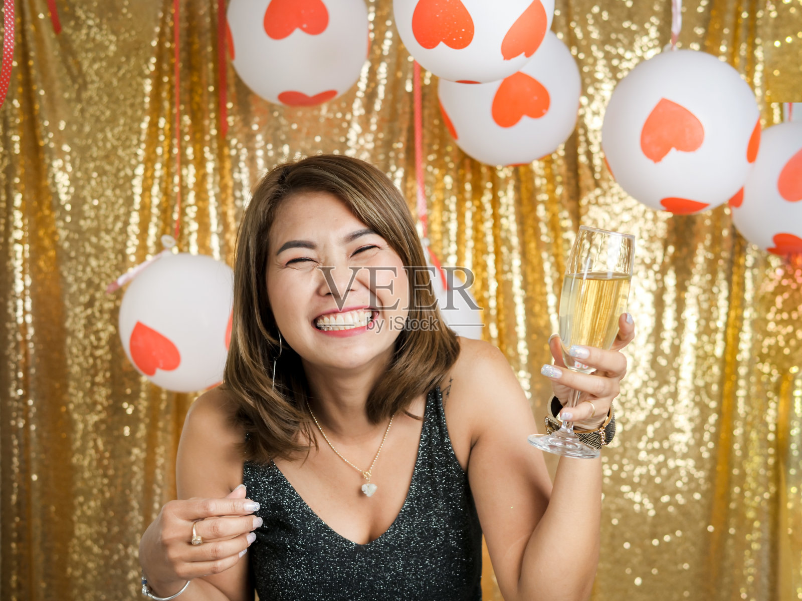 快乐的亚洲女人拿着“与金色闪闪的背景香槟杯。照片摄影图片