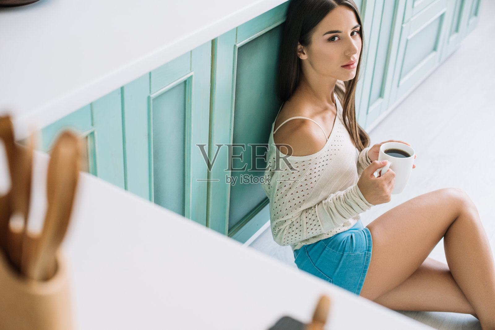 有魅力的年轻女人拿着咖啡坐在厨房的地板上照片摄影图片