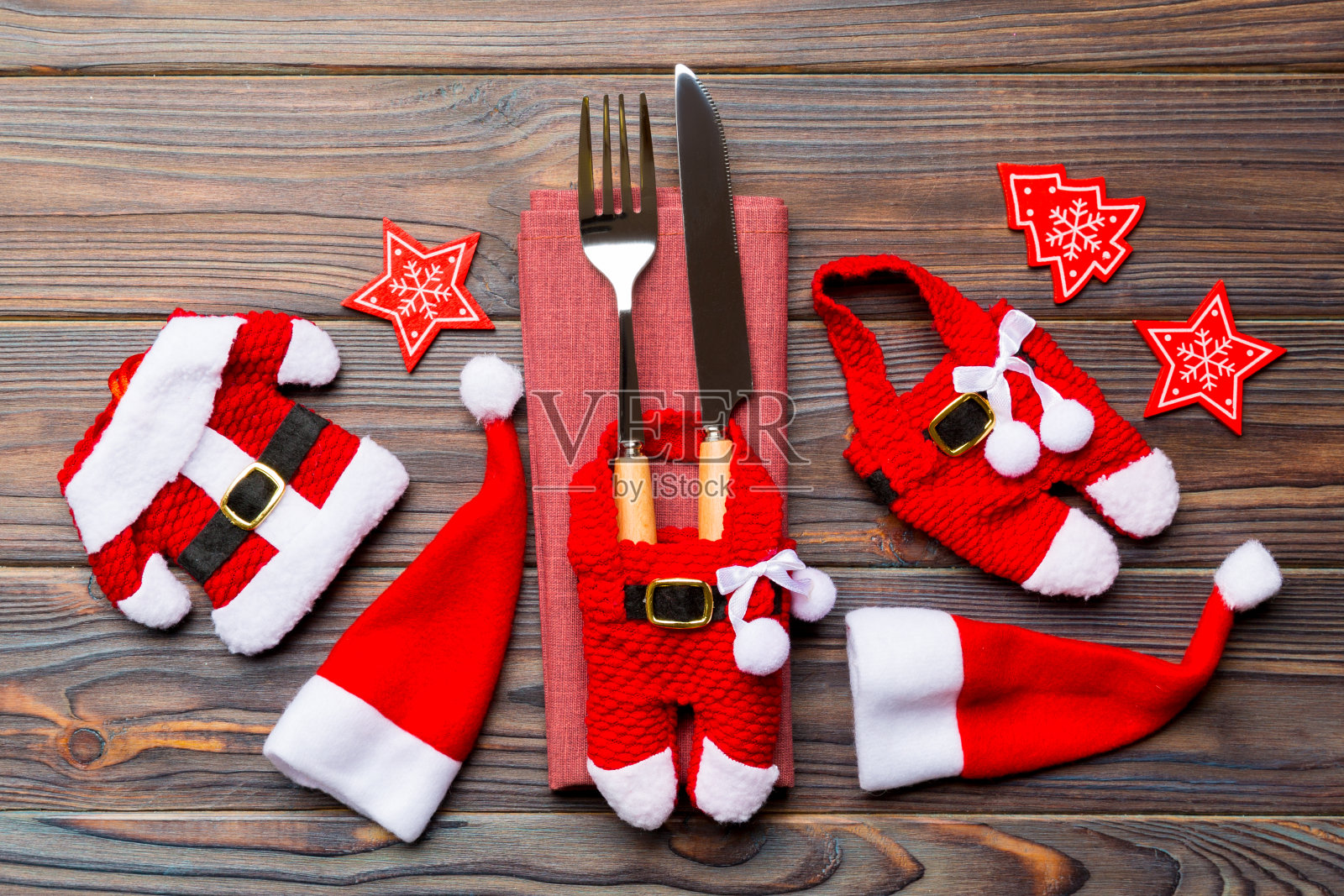 木制背景上的节日叉和刀。顶视图新年装饰品和圣诞老人的衣服和帽子。圣诞概念的特写照片摄影图片