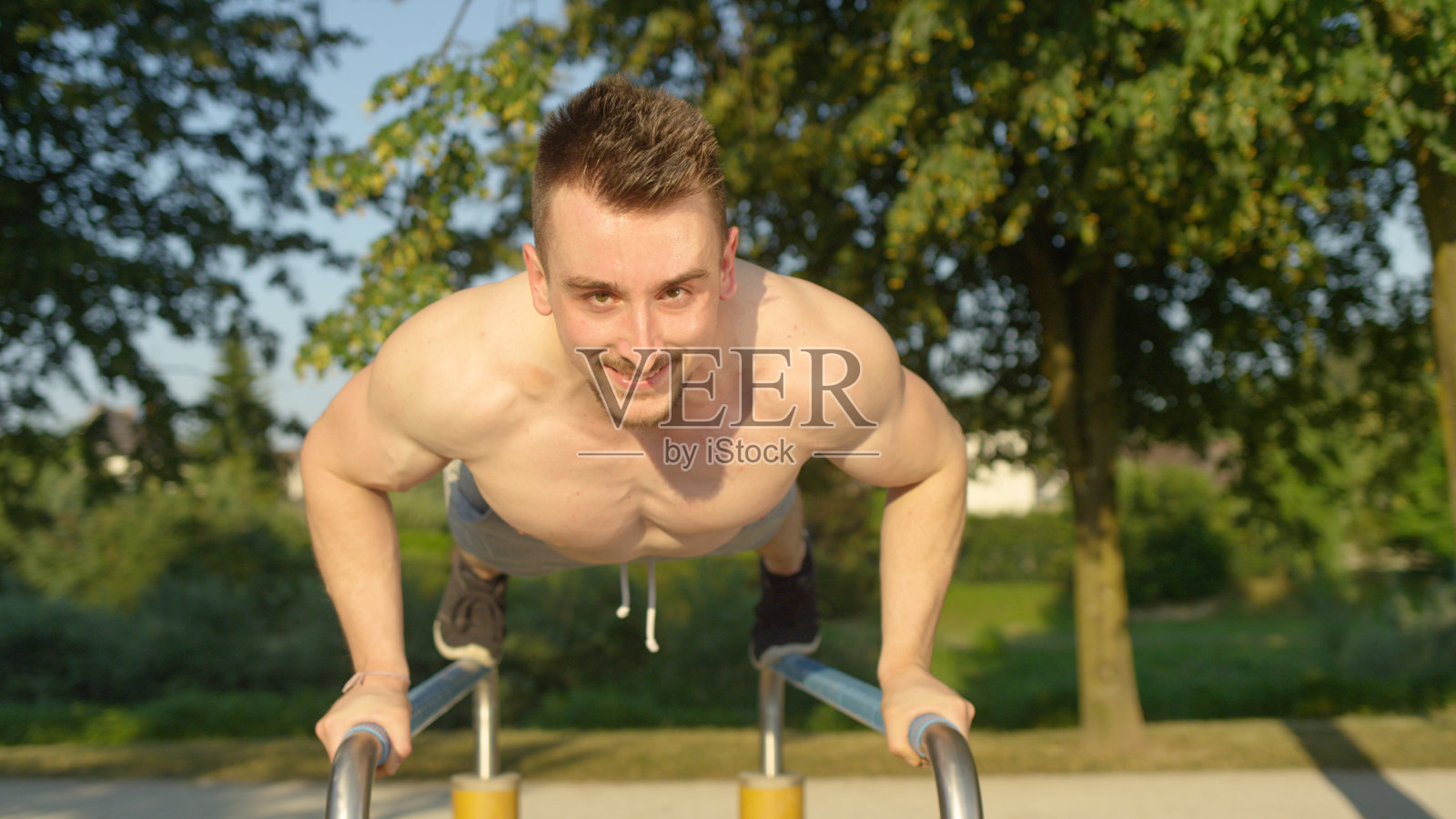 肖像:肌肉男在很棒的户外健身房里做双杠俯卧撑。照片摄影图片