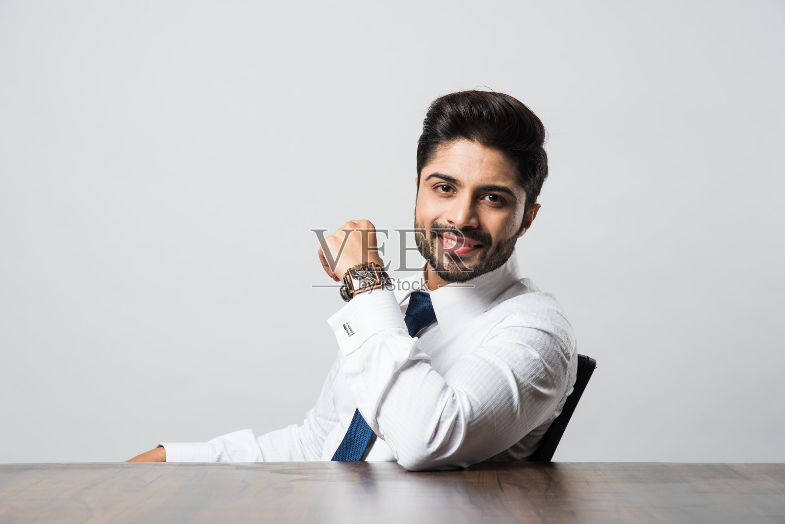 在灰色背景下，印度男性商人坐在办公室的桌子前照片摄影图片