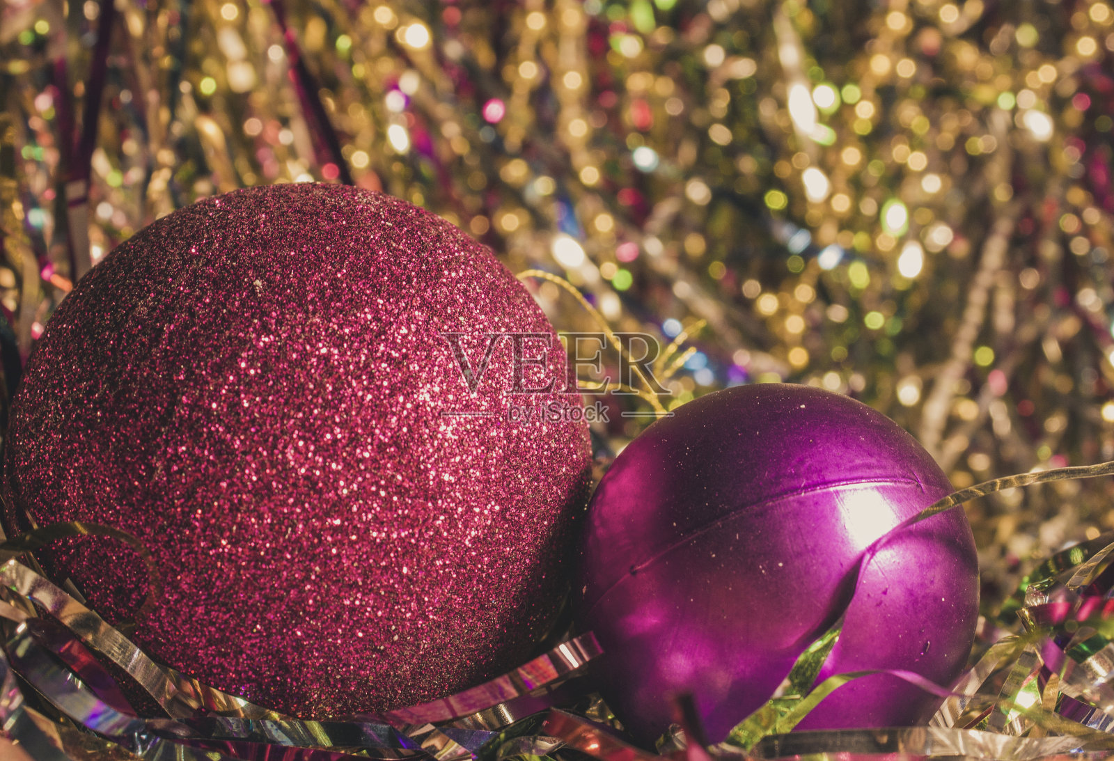 两个红色的圣诞球在闪闪发光的金属箔上。两个颜色相同大小不同的圣诞玩具。大的闪亮的红球和小的紫色的圣诞树照片摄影图片
