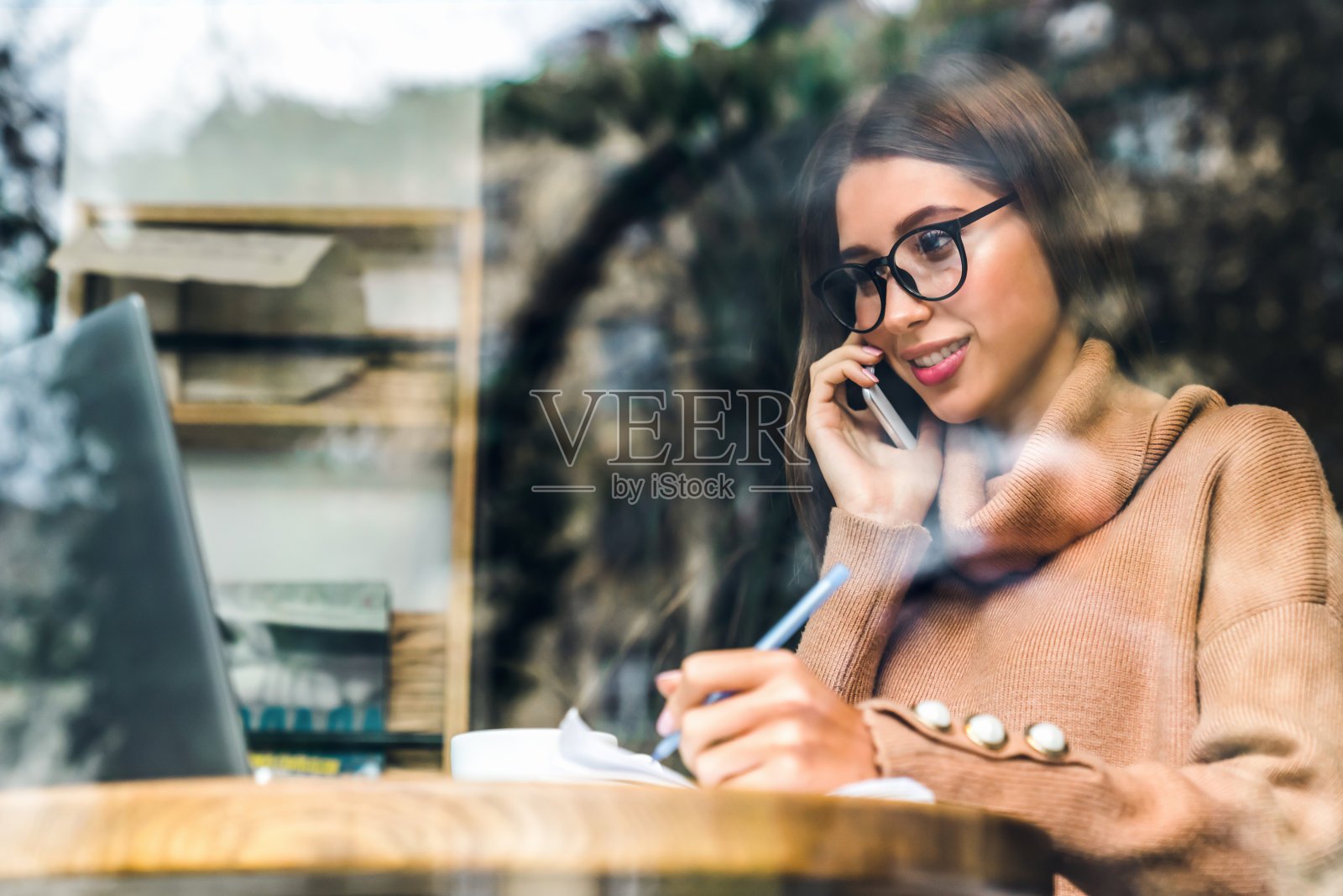 一个白人女性在咖啡店边打电话边用笔记本电脑工作。照片摄影图片