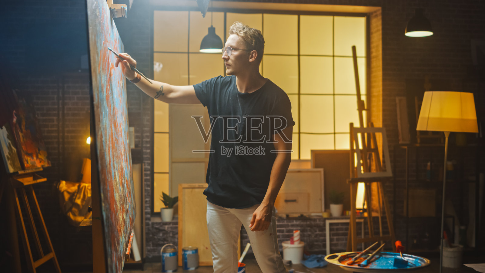 创作抽象画的天才艺术家的肖像，用画笔创作大胆的情感现代画。黑暗的创意工作室大帆布站在画架上照明。照片摄影图片