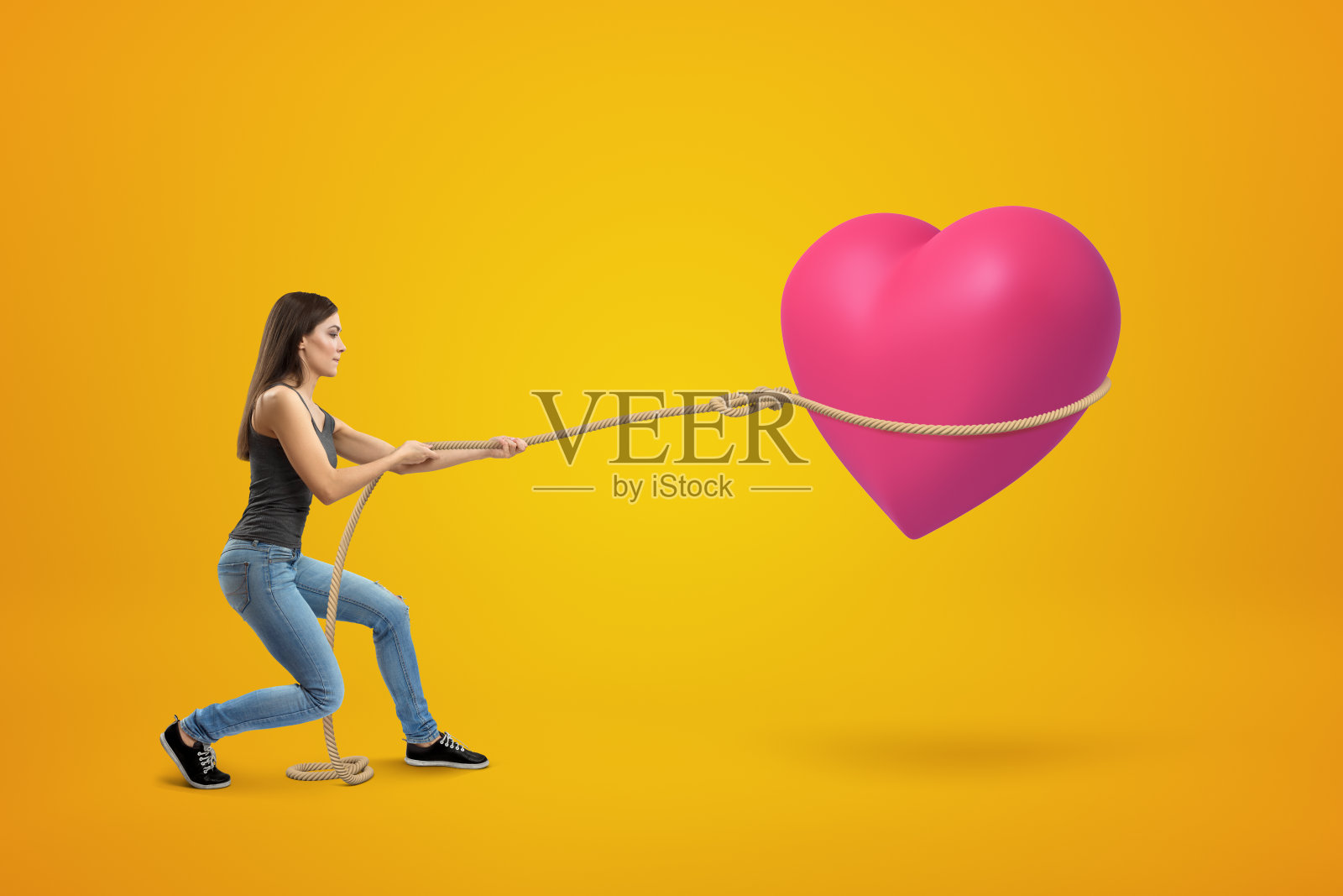 年轻的黑发女孩穿着休闲牛仔裤和t恤套索大粉红色的心在黄色的背景照片摄影图片