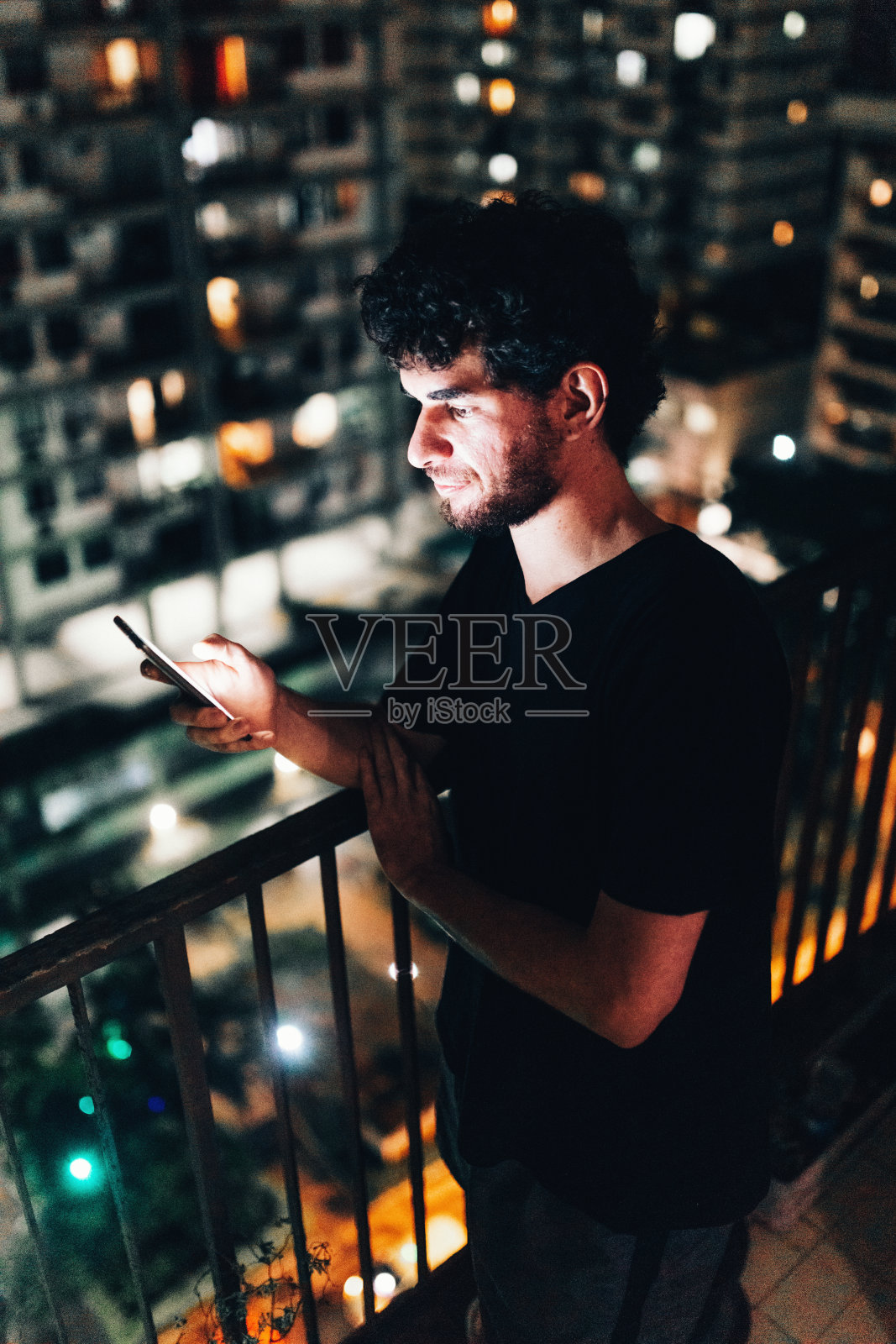 年轻人晚上在住宅阳台上用智能手机照片摄影图片