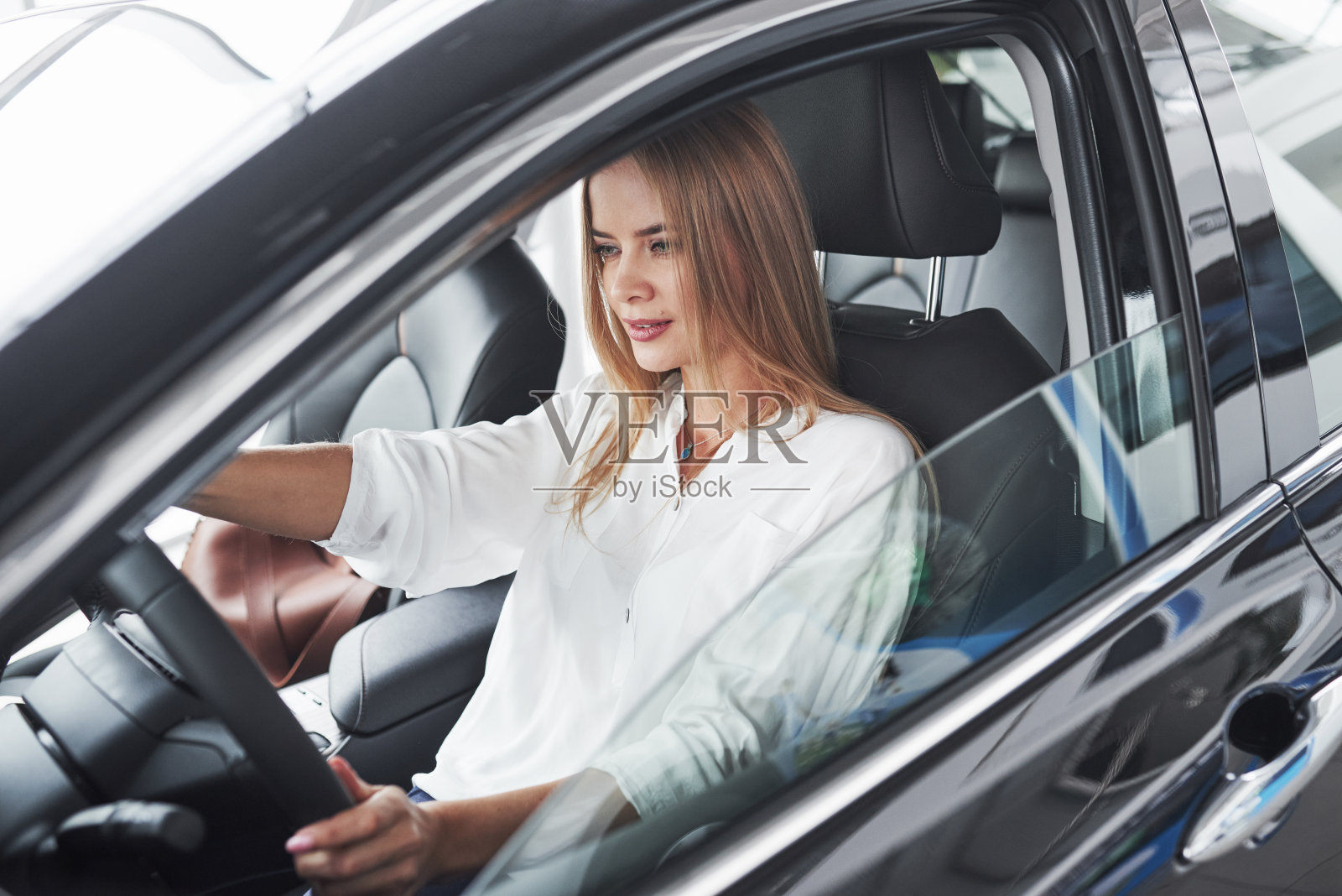 看起来简单。漂亮的金发女孩坐在有现代黑色内饰的新车里照片摄影图片