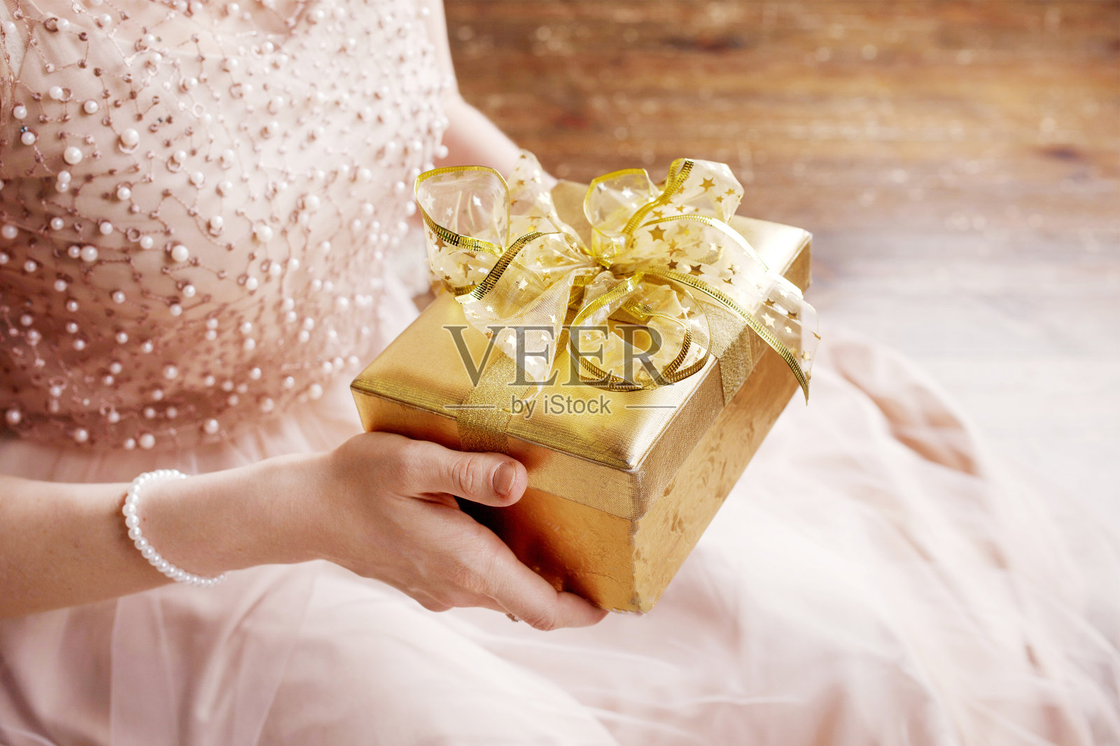 女人的手拿着金礼盒。圣诞节、新年、生日概念。节日背景与散景和阳光。神奇的童话故事照片摄影图片