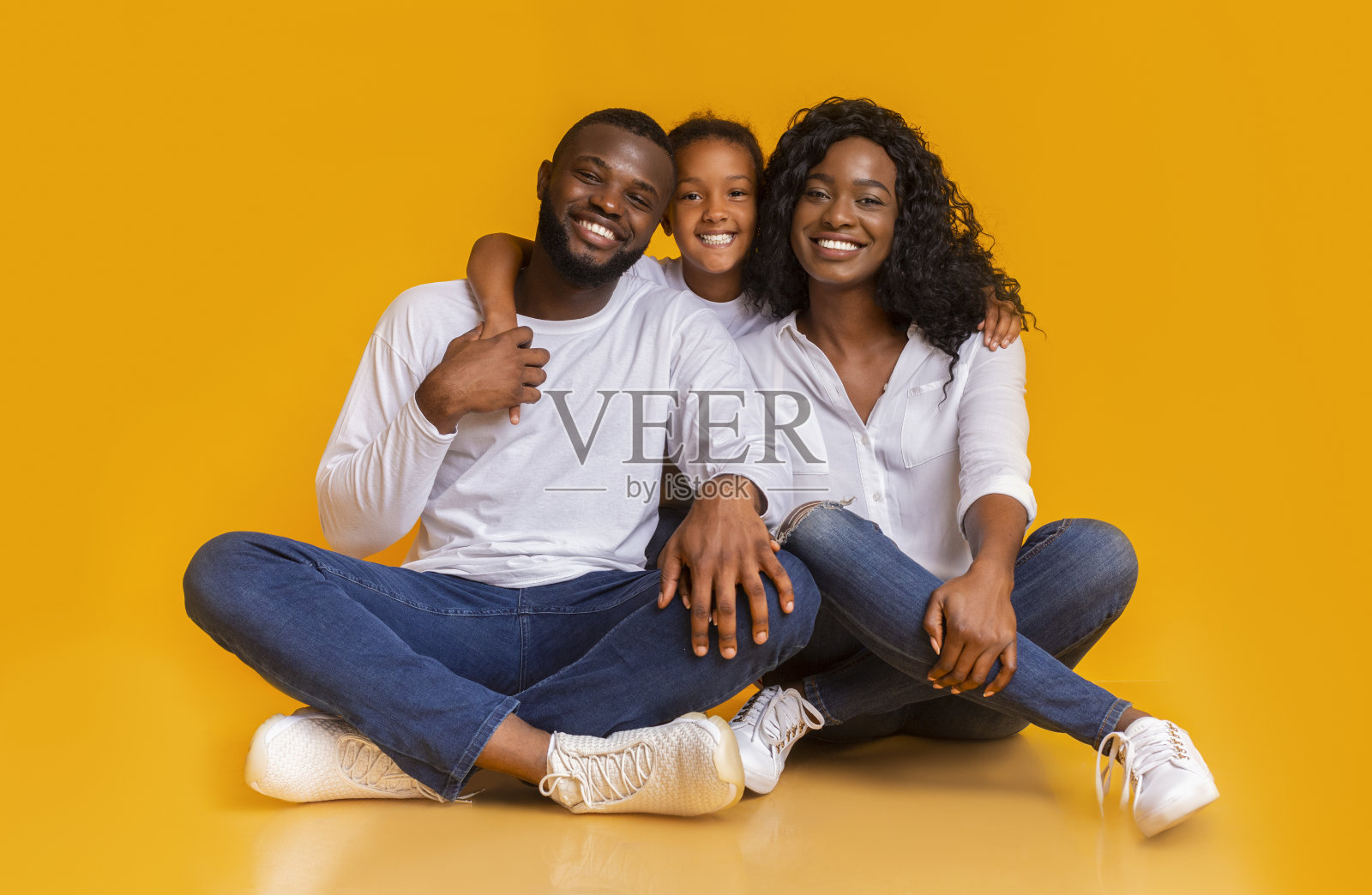 父母和女儿坐在地板上，看着黄色背景下的摄像机照片摄影图片