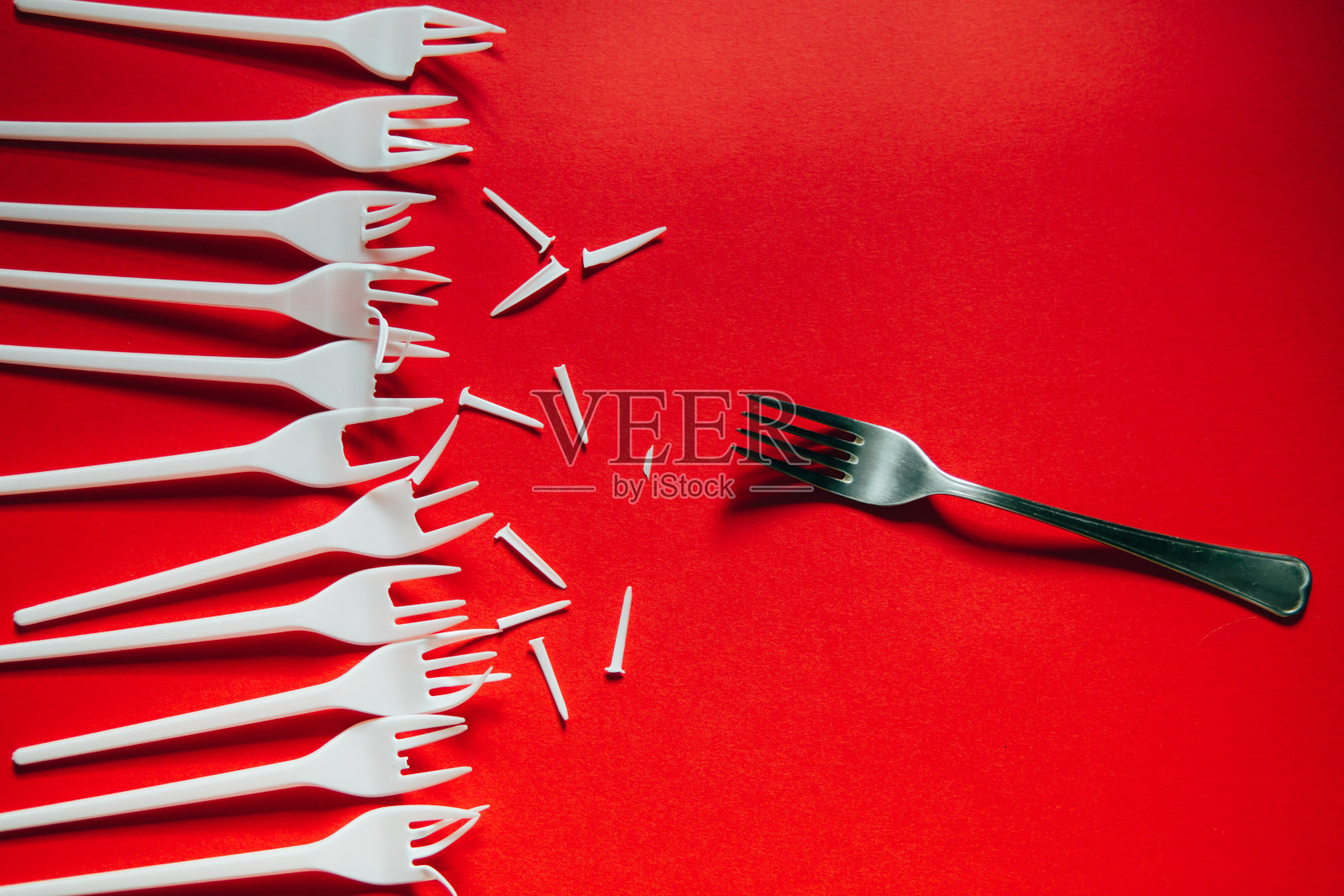 红色背景上有很多塑料叉子和一种金属。照片摄影图片