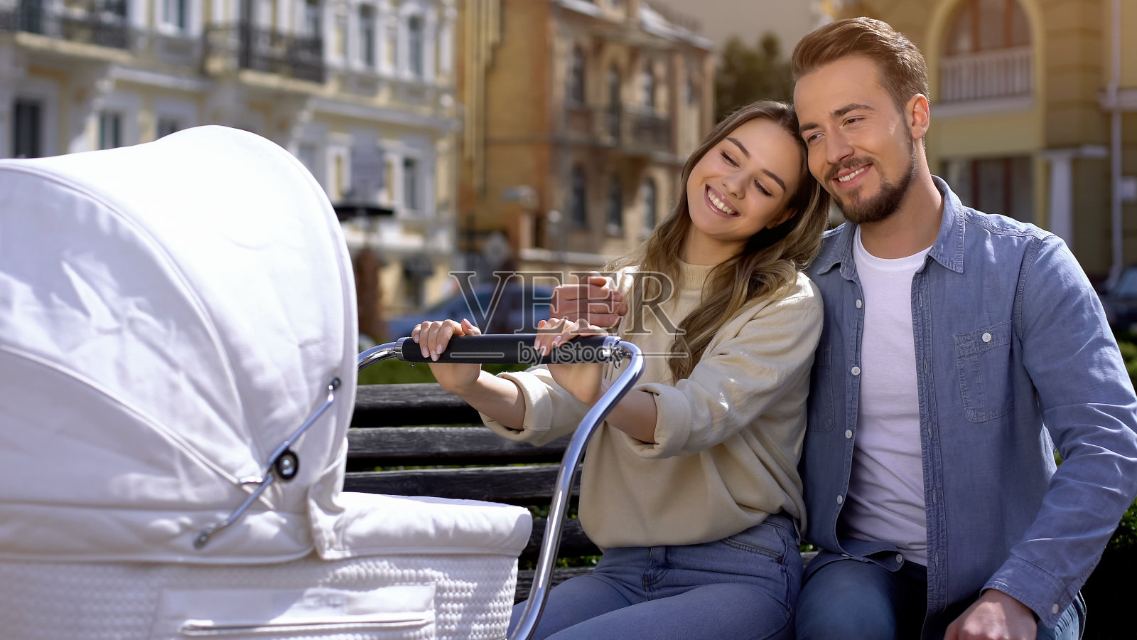 快乐的年轻夫妇坐在长椅公园的马车上欣赏婴儿，家庭的爱照片摄影图片