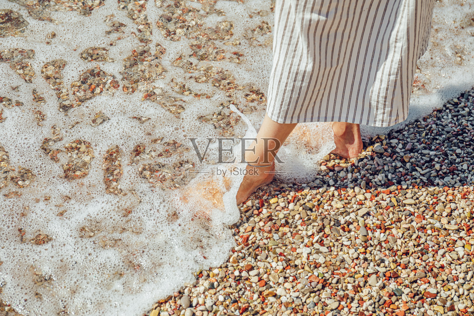 美丽的女人的腿在卵石海滩和泡沫海水照片摄影图片