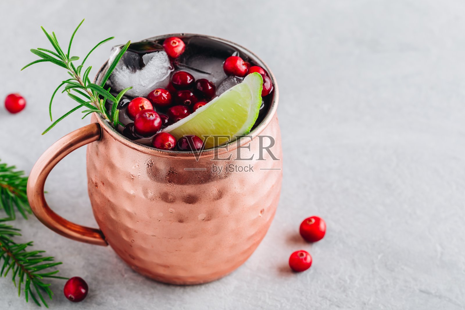 莫斯科骡子假日冰鸡尾酒铜杯与蔓越莓，酸橙和迷迭香的石头背景。照片摄影图片