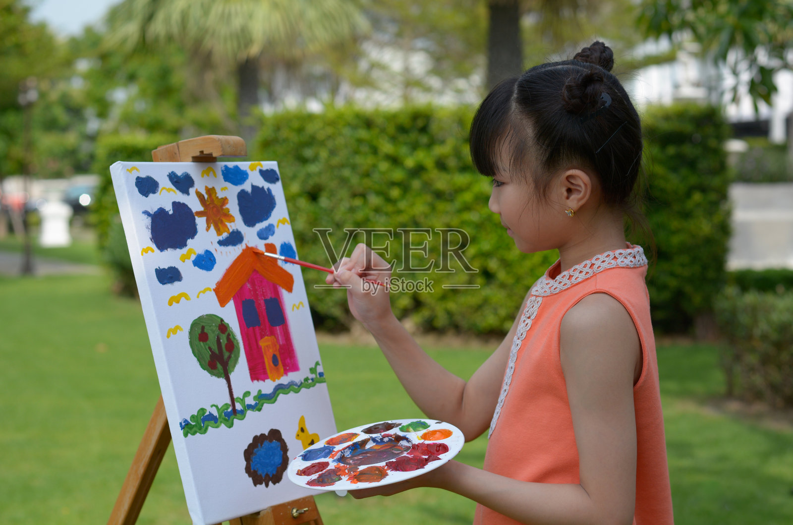 这个年轻的亚洲女孩正在前院的白画布上享受绘画的乐趣。照片摄影图片