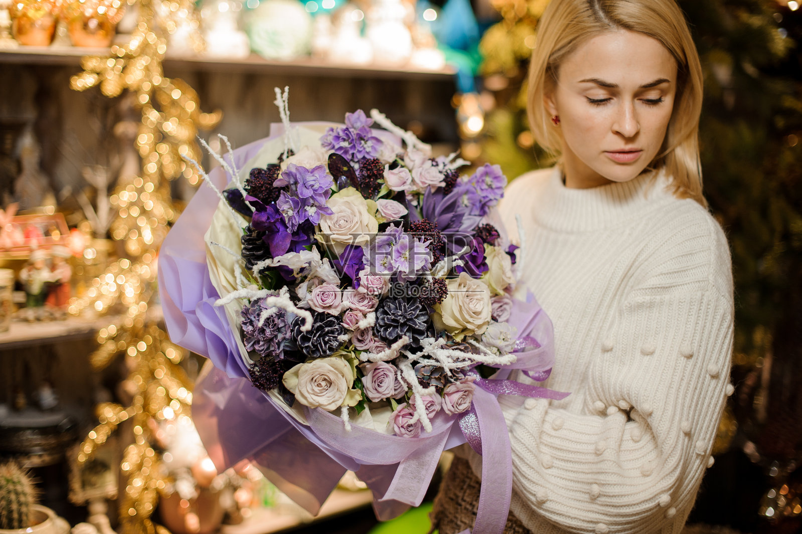 一名年轻女子手持一束紫色和奶油色的花，上面装饰着黑色的球果照片摄影图片