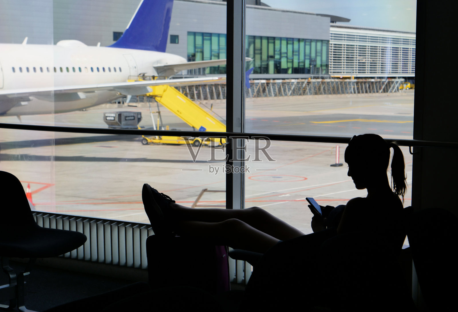 剪影女游客在等待她的航班和玩手机游戏照片摄影图片