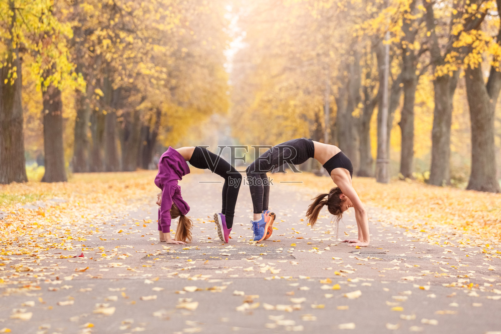 户外休闲。姐妹们在秋天的公园里做足弓运动照片摄影图片