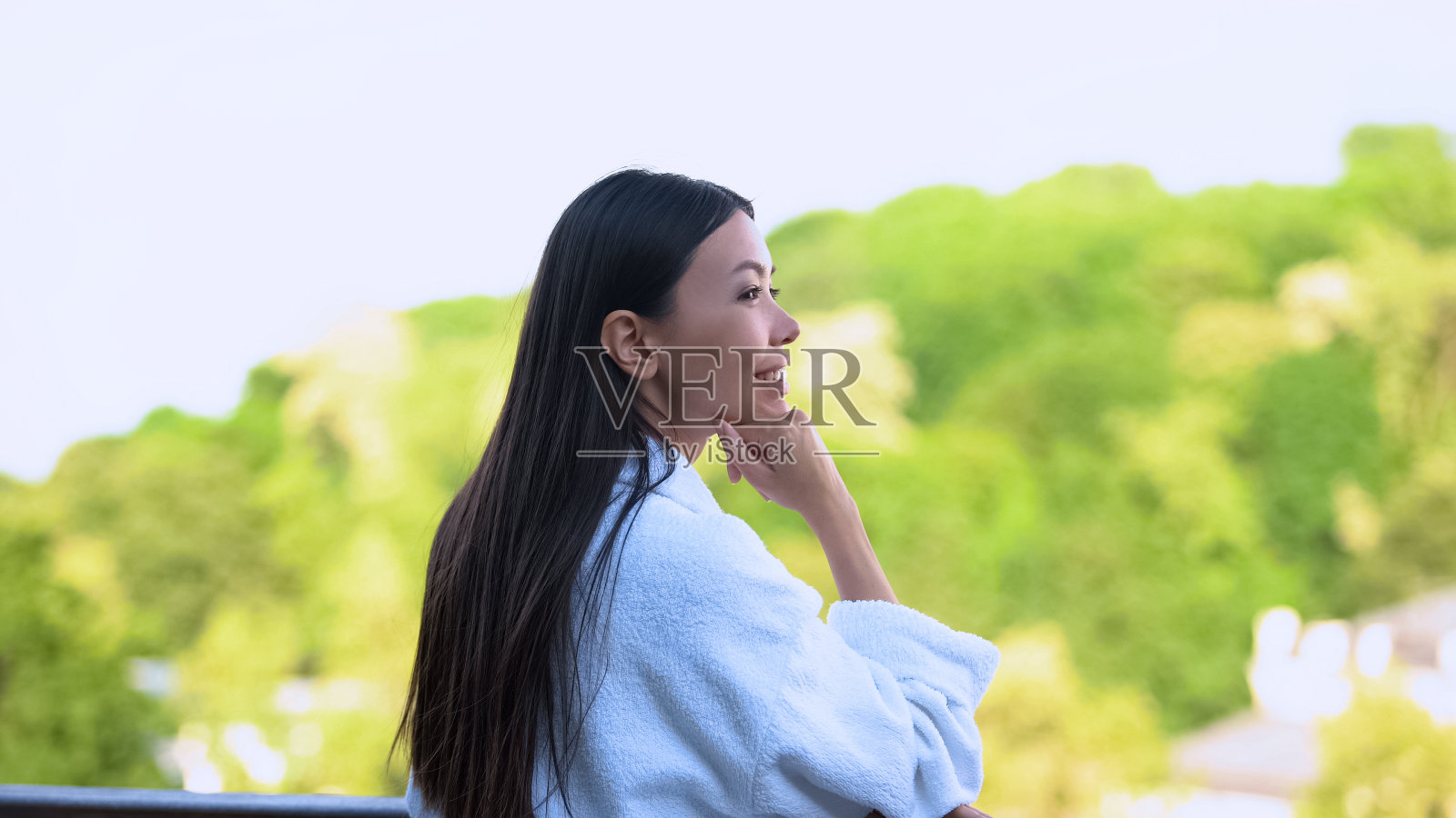快乐的女人穿着酒店浴袍站在酒店阳台上欣赏自然风光照片摄影图片