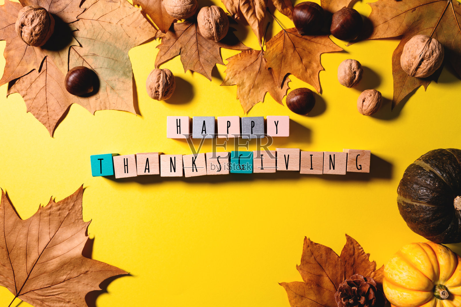 用枫叶、坚果、南瓜和木头方块作黄色的背景，祝你感恩节快乐照片摄影图片