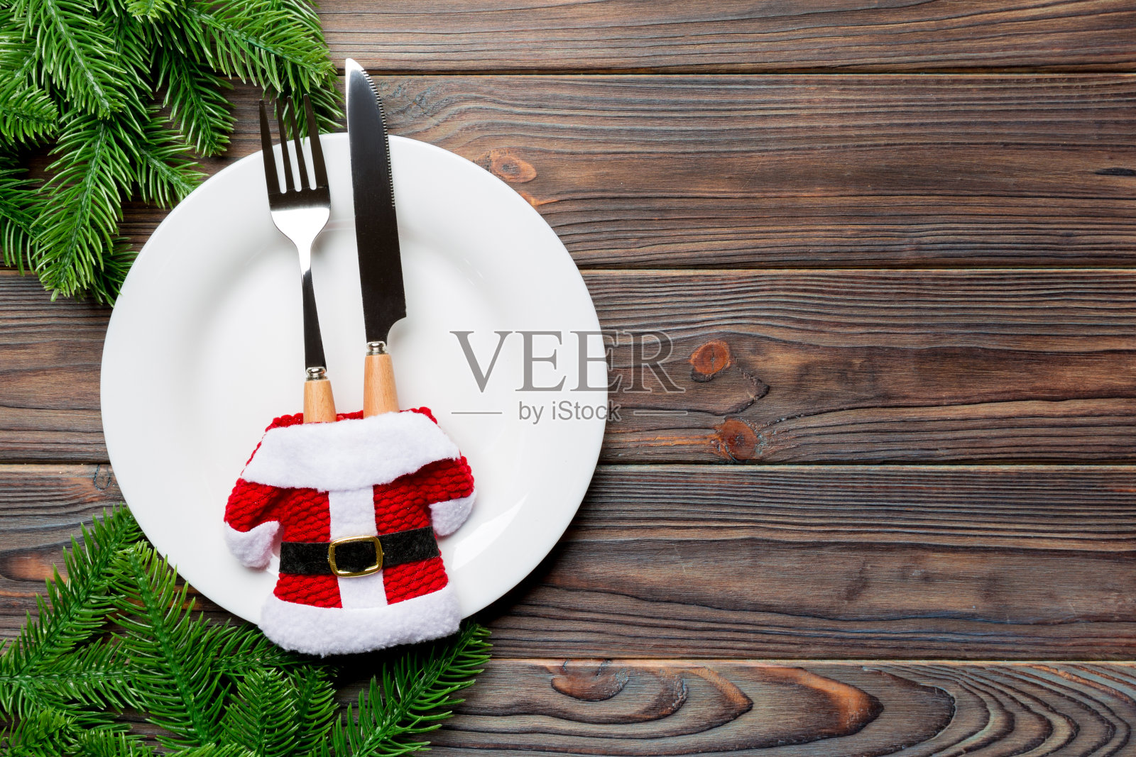 用木制背景装饰圣诞老人衣服的盘子和餐具组成的节日组合。顶视图的圣诞装饰与空空间为您的设计。节日的时间概念照片摄影图片