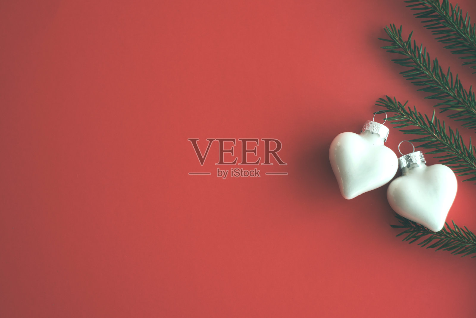 艺术圣诞贺卡。圣诞树白色玻璃玩具两颗心和天然杉木树枝上的云杉红纸。照片摄影图片