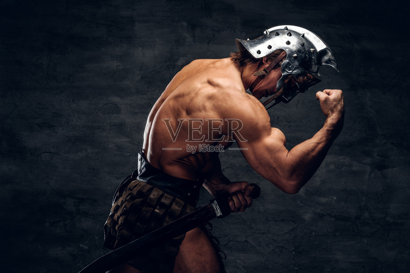 强壮的赤膊角斗士戴着头盔正在显示他的肌肉照片摄影图片