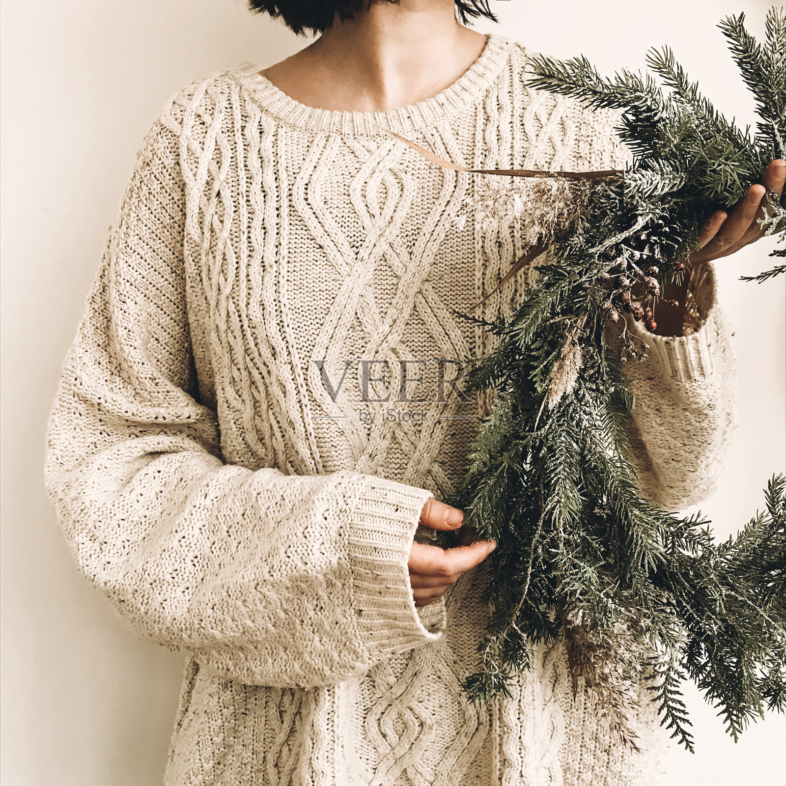 女孩手里拿着时髦的乡村花环。嬉皮士女孩在针织毛衣抱着农村现代花环在白色的墙壁背景。节日装饰。手机照片照片摄影图片