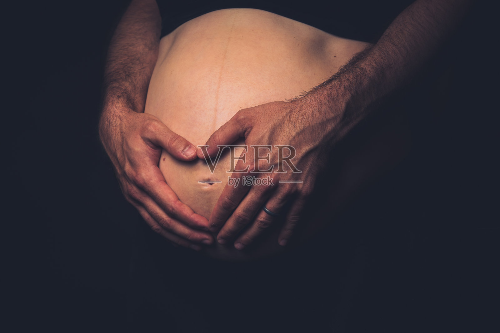 黑色背景上的孕妇和男子手持心形图案。照片摄影图片