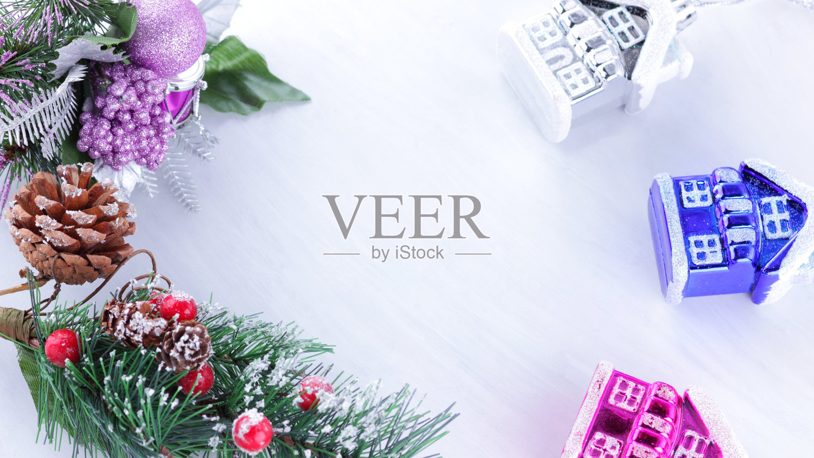 冷杉树枝上的节日装饰。白色背景上的圣诞装饰。杉树枝上的松果和红色浆果。紫色的球和五颜六色的玩具房子。宽屏照片摄影图片