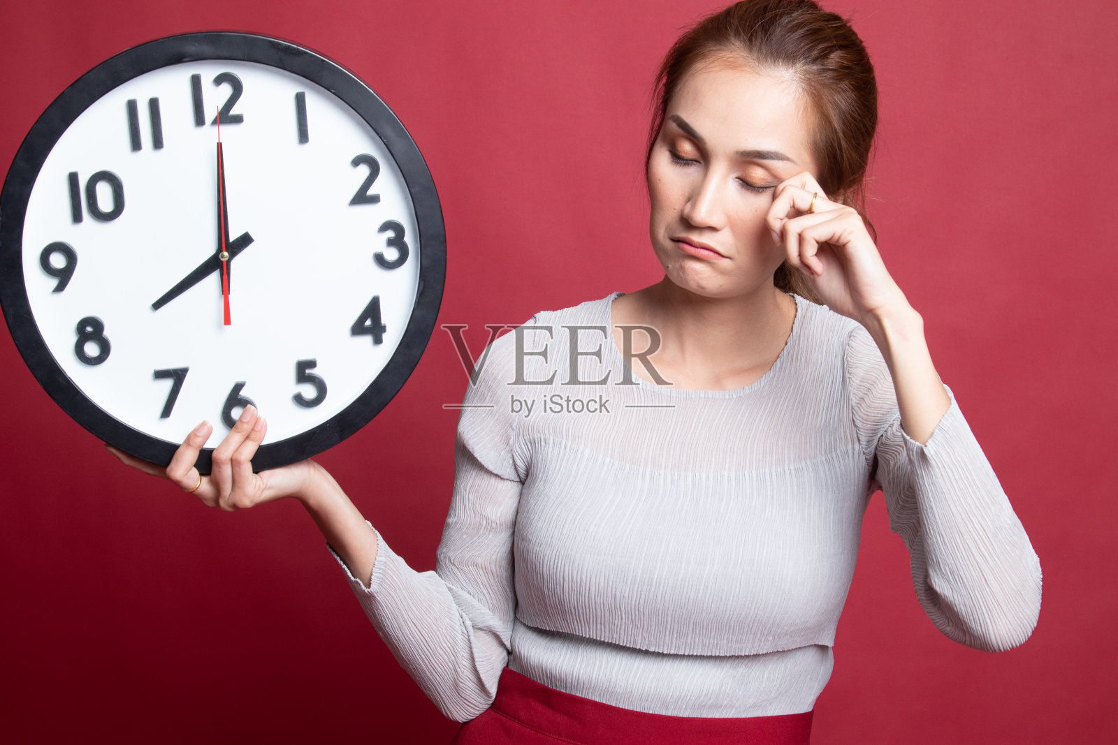 睡眼惺忪的年轻亚洲女人早上拿着钟。照片摄影图片