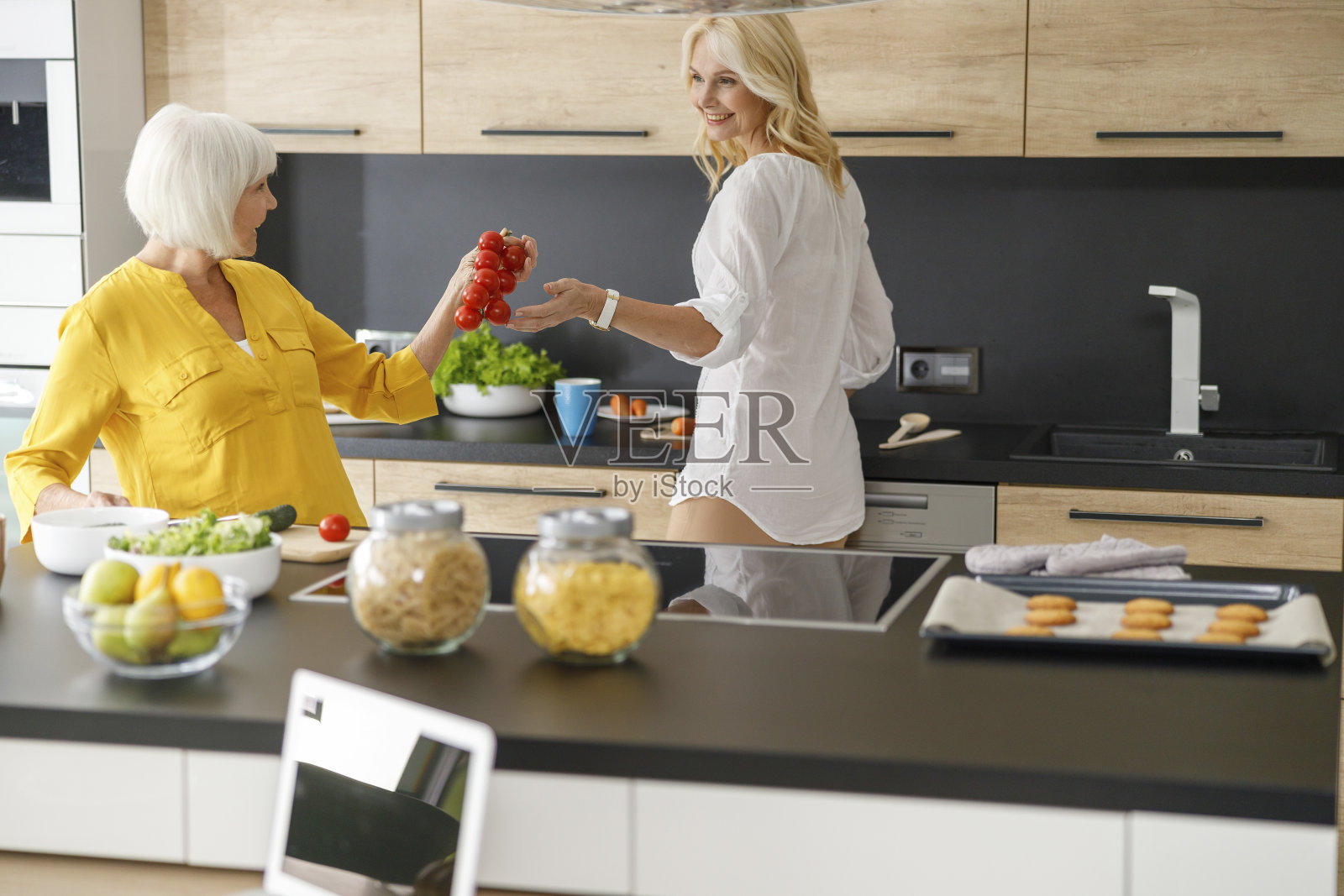 快乐的成年女人在厨房里拿着西红柿照片摄影图片