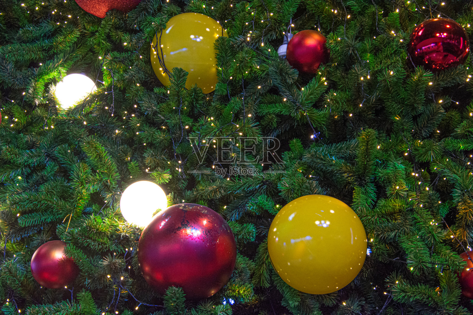 彩灯装饰的圣诞树上挂着黄色和红色的球。照片摄影图片