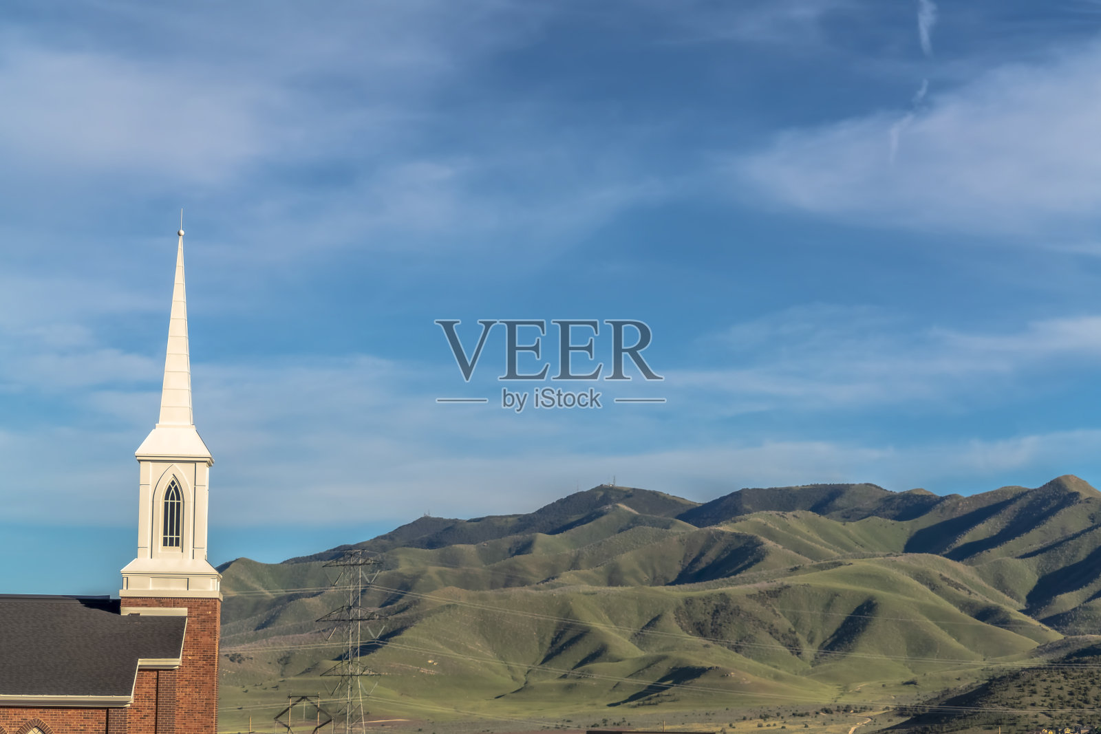 一座教堂的屋顶和尖顶，背对着电线、山脉和蓝天照片摄影图片