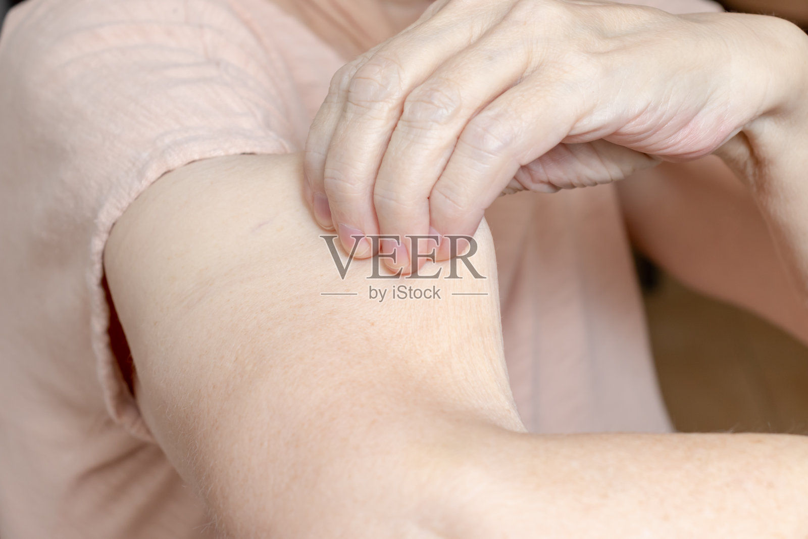 一位老年妇女抱着，拉着她手臂上的皮肤，皮肤非常松弛照片摄影图片