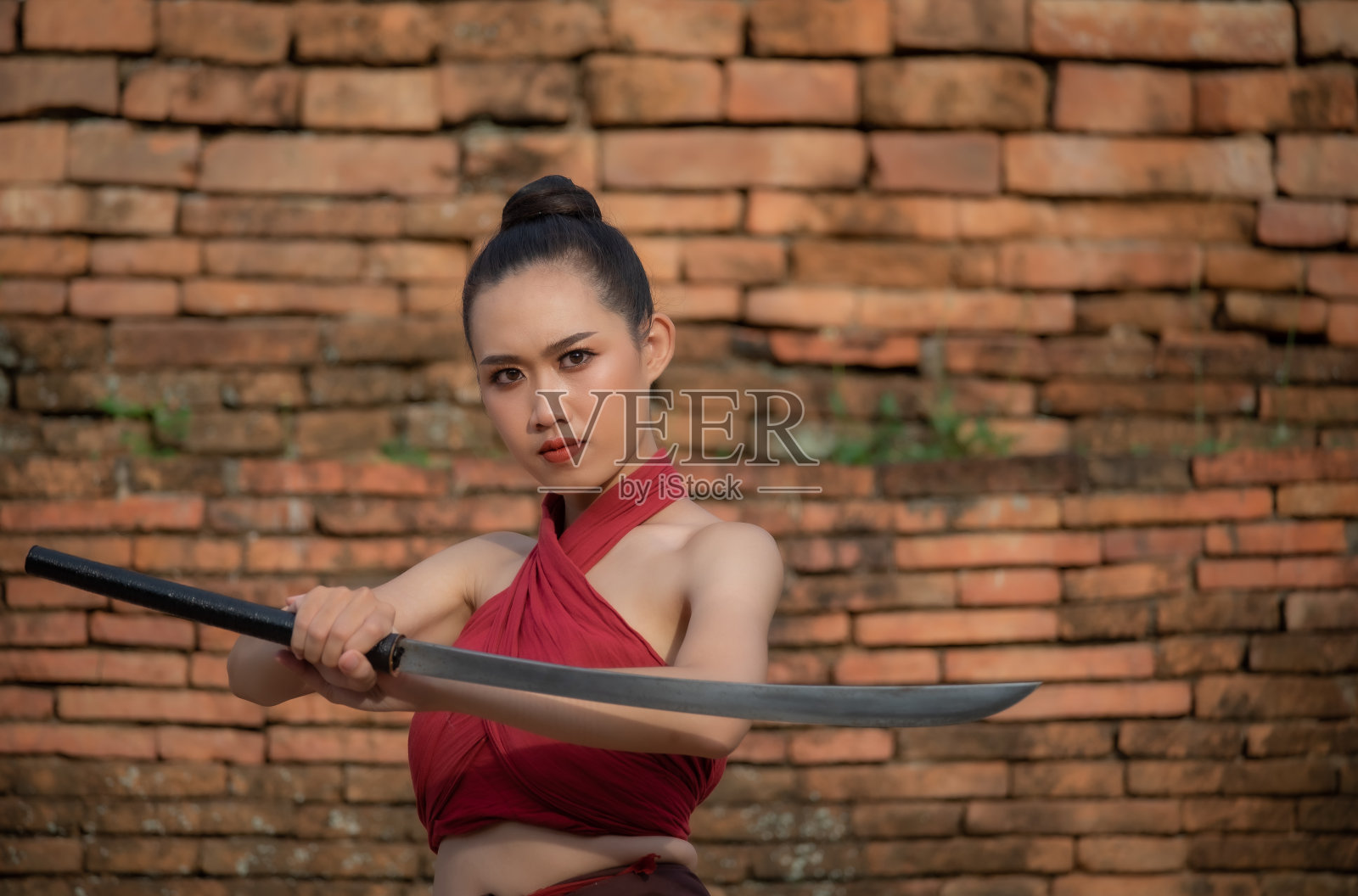 一个穿着红衣服的漂亮女孩拿着一把剑在古庙里。照片摄影图片