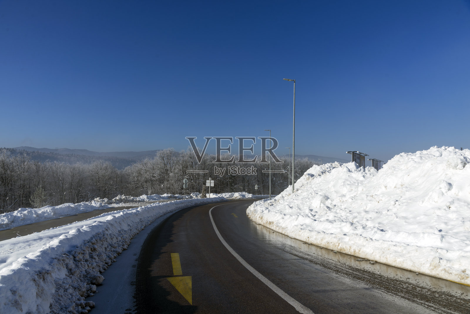 冬天的雪路景象，有白雪皑皑的树木、岩石和柏油路。照片摄影图片