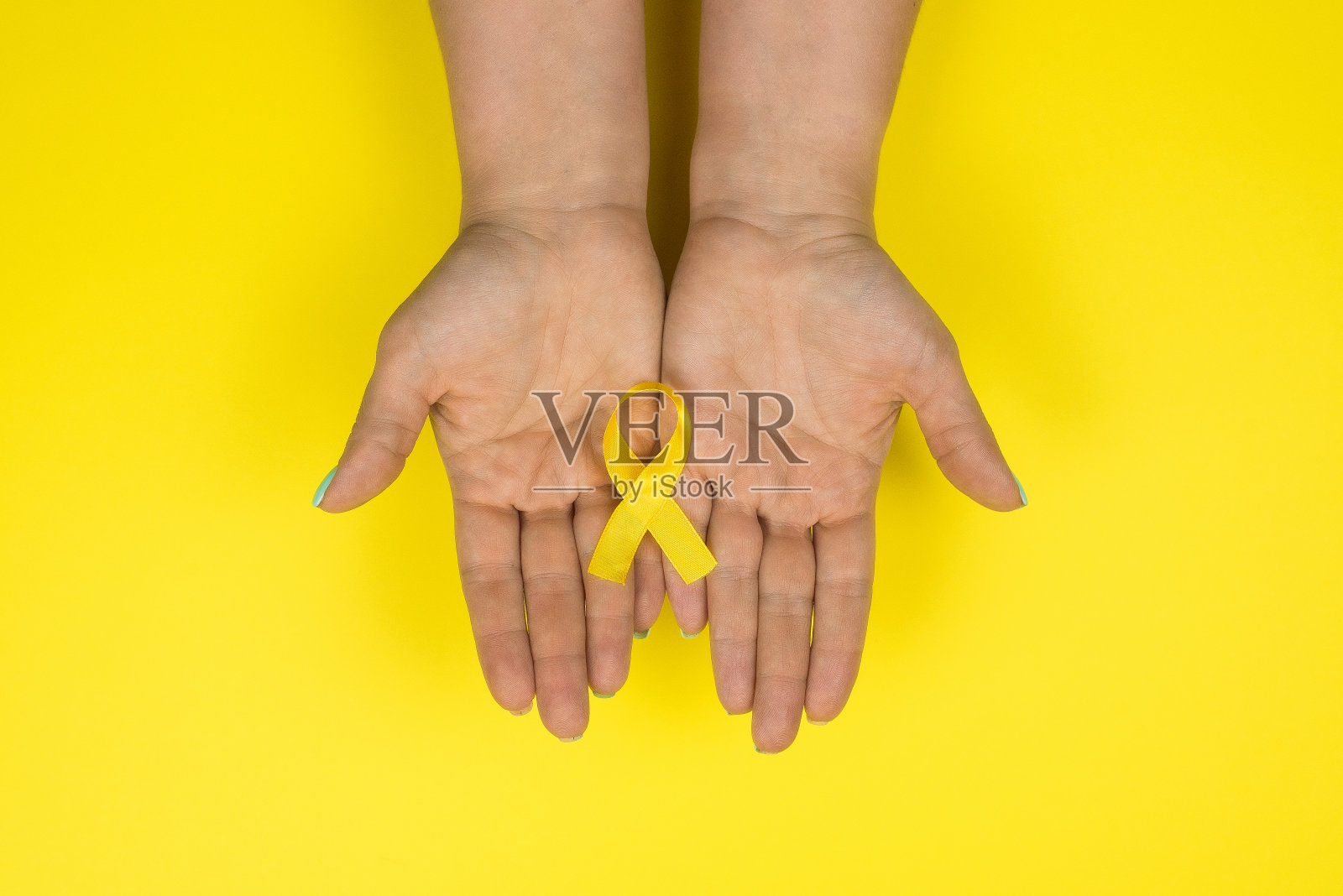 黄色的金色丝带在一个女孩的手中以黄色为背景。儿童癌症的概念。宣传月。儿童癌症日2月15日照片摄影图片