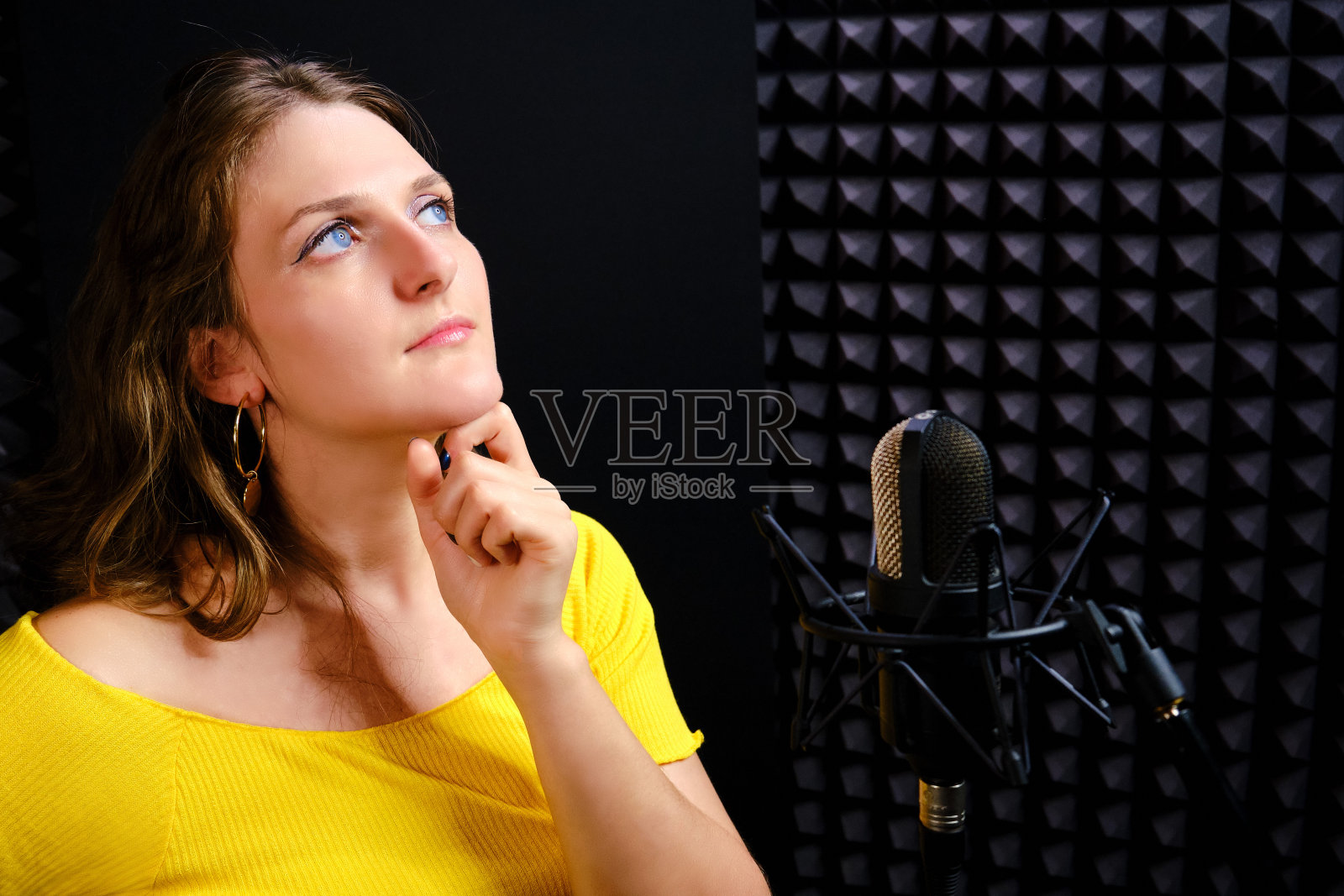 歌手陷入了沉思，站在麦克风前，拷贝空间。在录音棚录制歌曲时歌手的反映。年轻女子把手放在黑色背景下的下巴上。照片摄影图片