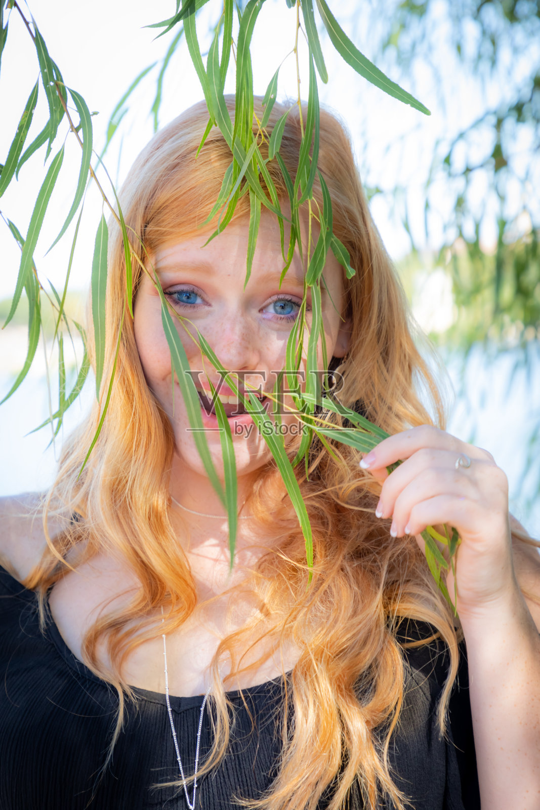 一个美丽的微笑少女的肖像与红头发在户外躲在树叶后面照片摄影图片