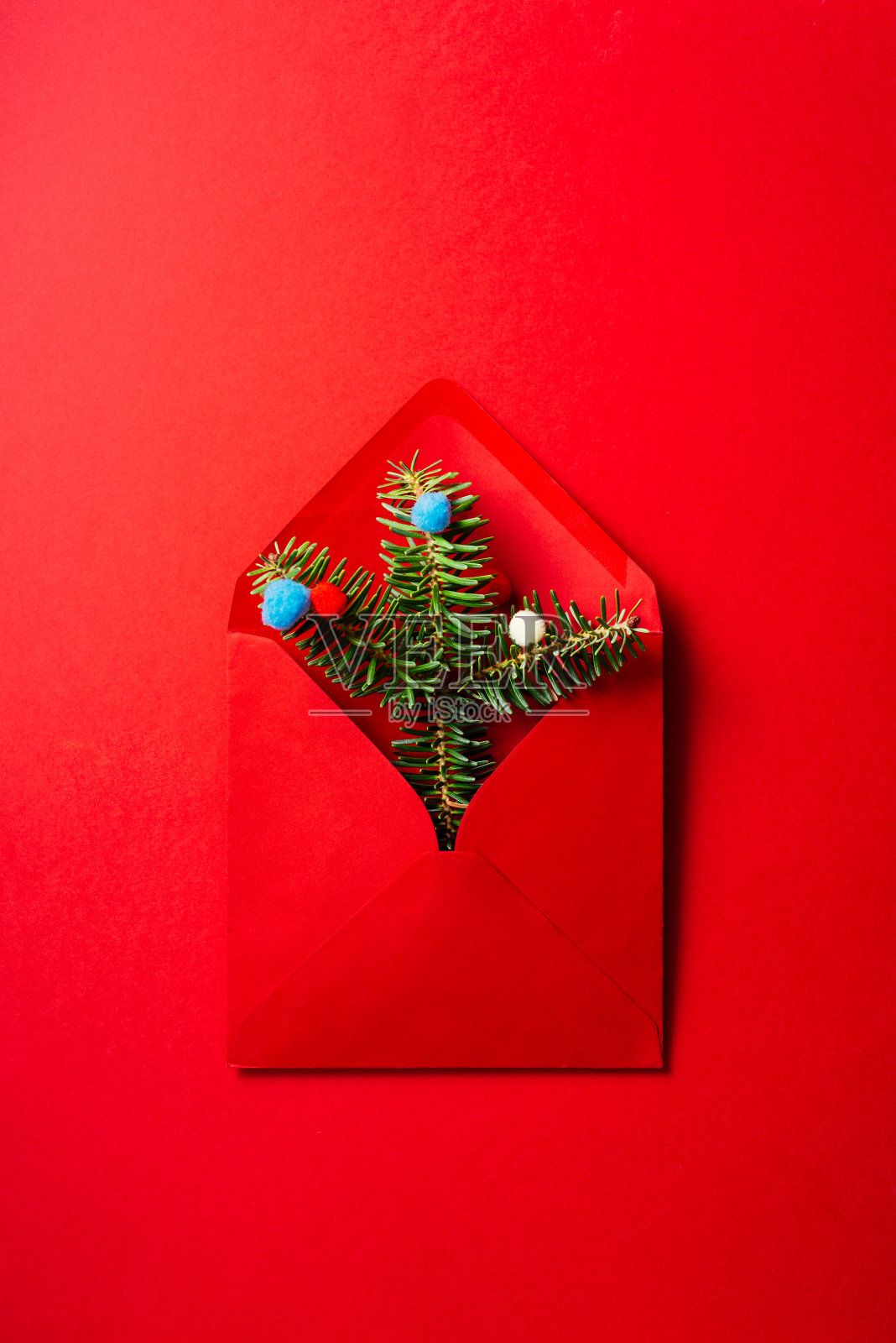圣诞组成。红色信封与冷杉树枝和彩色羊毛球在红色的背景。照片摄影图片
