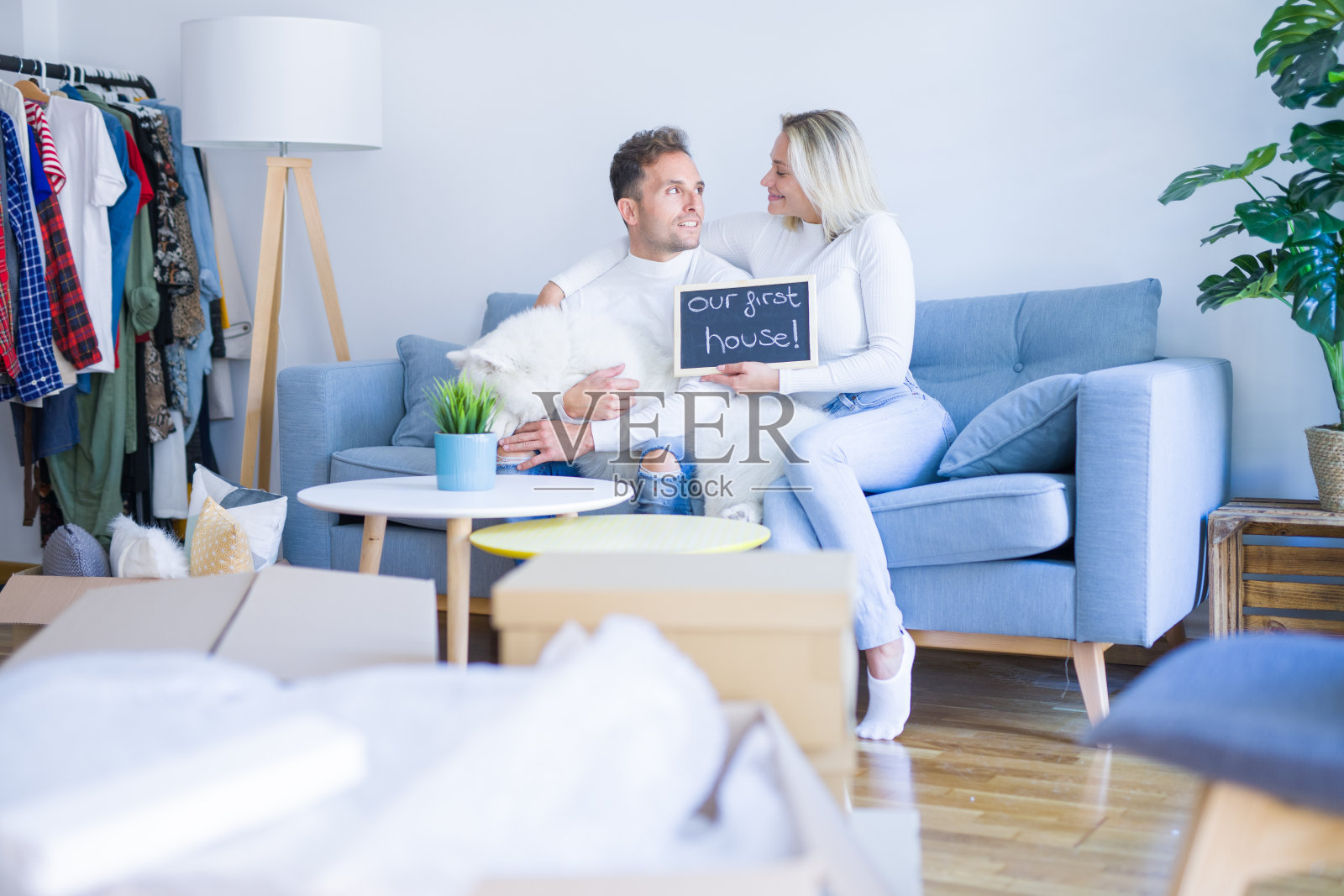 年轻漂亮的夫妇和狗坐在沙发上拿着黑板在新家周围的纸板箱留言照片摄影图片