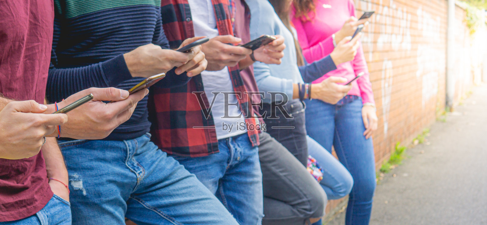 一排千禧一代的年轻朋友在看智能手机。阳光的效果。照片摄影图片