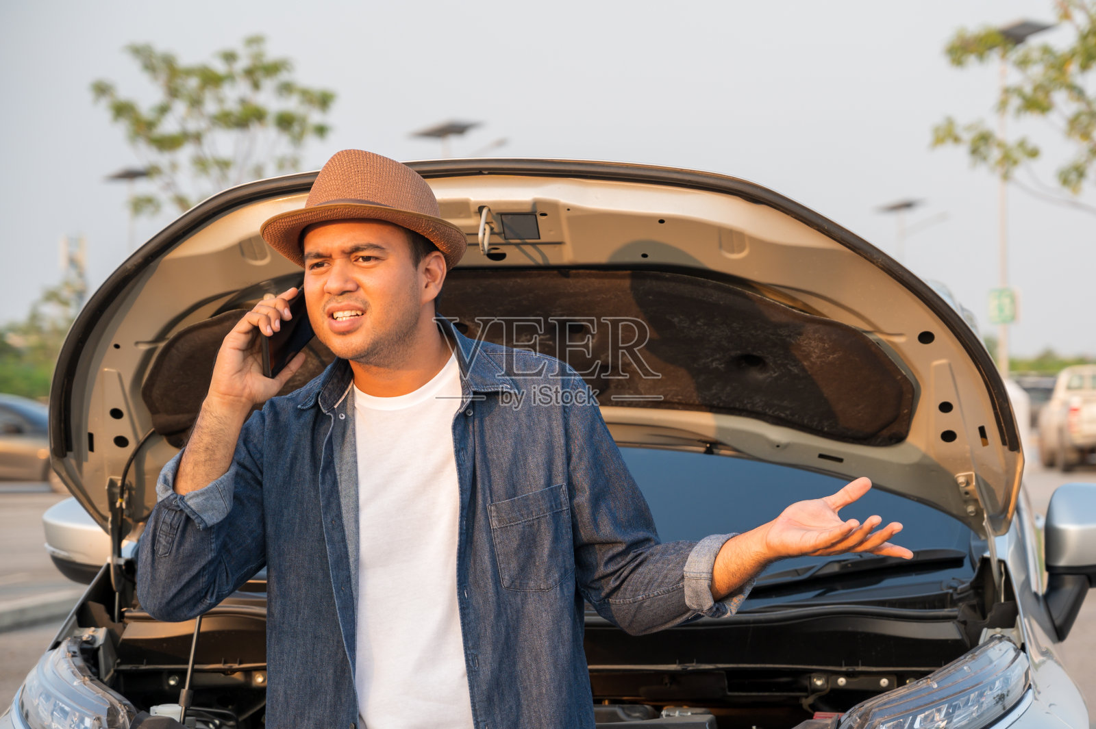一位年轻的亚洲游客开着一辆车，在路上抛锚了。他下来查看引擎盖，然后打电话给修理工寻求帮助。照片摄影图片